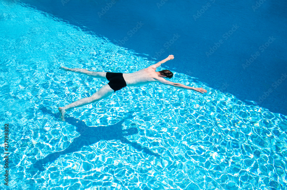 Man in black trousers swimming slowly in a swimming pool on a hot sunny day