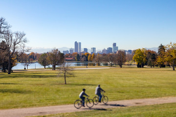 Denver Colorado downtown skyline with people riding bicycles on a trail through City Park and snow capped mountains in the background