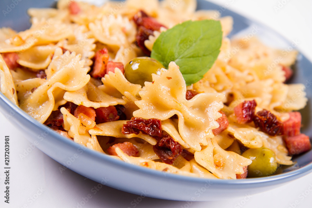 Farfalle pasta with sun dried tomato, ham and olives decorated with fresh mint Farfalle pasta with sun dried tomato, ham and olives decorated with fresh mint