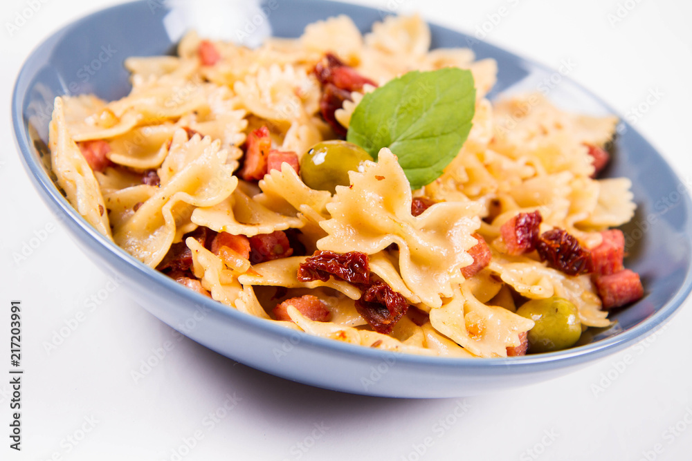 Farfalle pasta with sun dried tomato, ham and olives decorated with fresh mint