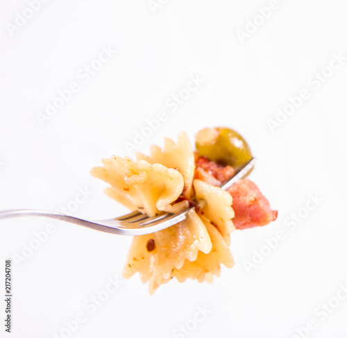 Farfalle pasta with sun dried tomato, ham and olives on a fork on a white background
