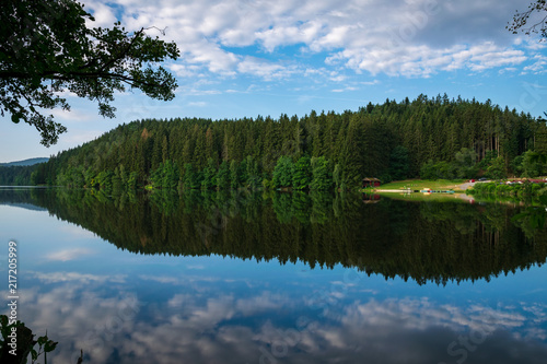 Fototapeta Naklejka Na Ścianę i Meble -  Lake with Reflection on the Water and Trees in the background and Clouds on the sky in the bavarian forest