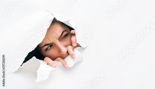 Portrait of a woman looking through the hole in white paper. Distrustful look. Women's curiosity and gossip. A jealous wife. photo