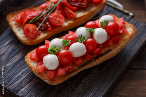 Bruschetta with tomato, basil and mozzarella cheese on wooden board. Traditional italian appetizer or snack, antipasto photo