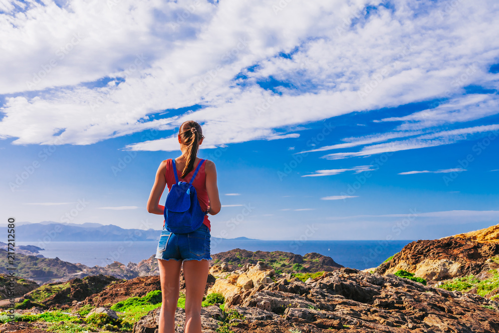 Tourist woman with backpack on Cap de Creus, natural park. Eastern point of Spain, Girona province, Catalonia. Famous tourist destination in Costa Brava. Sunny summer day with blue sky and clouds