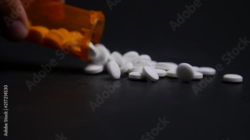 Hand Pours Out Bottle Of Pills On To Table In Slow Motion photo