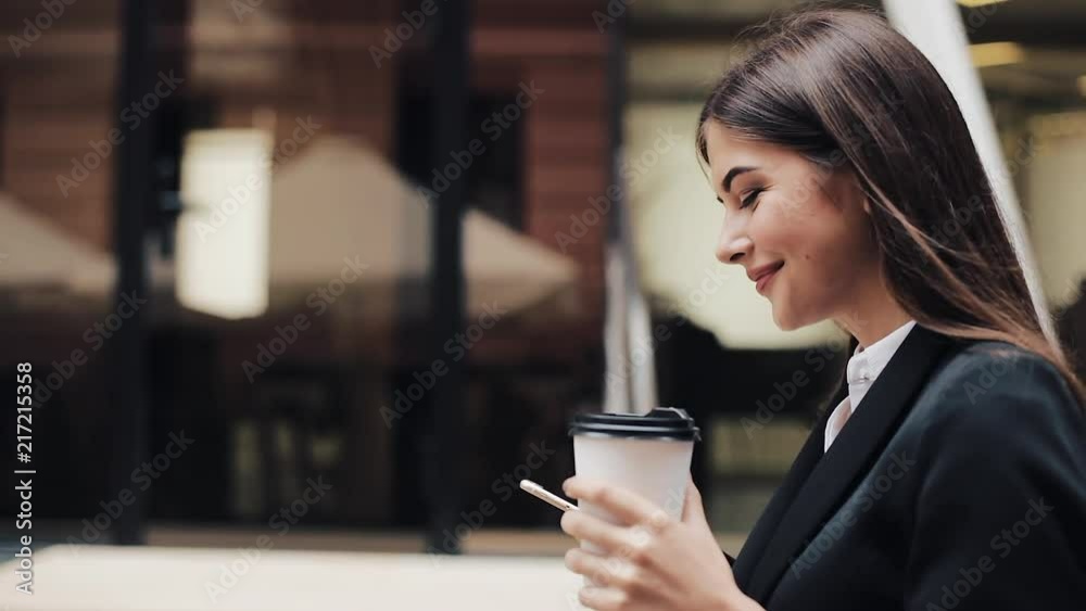 Professional young businesswoman walking on urban street using smartphone and drink coffee. Concept: new business, communication, banker. Outside, slow motion Professional young businesswoman walking on urban street using smartphone and drink coffee. Concept: new business, communication, banker. Outside, slow motion