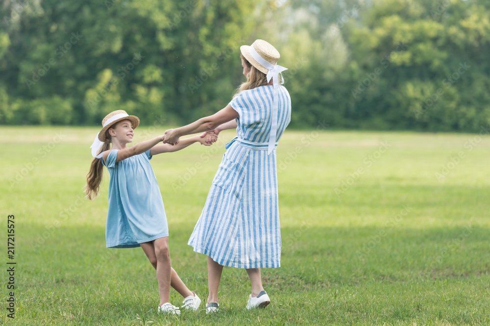 Naklejka premium mother and daughter holding hands, twisting and having fun on green lawn
