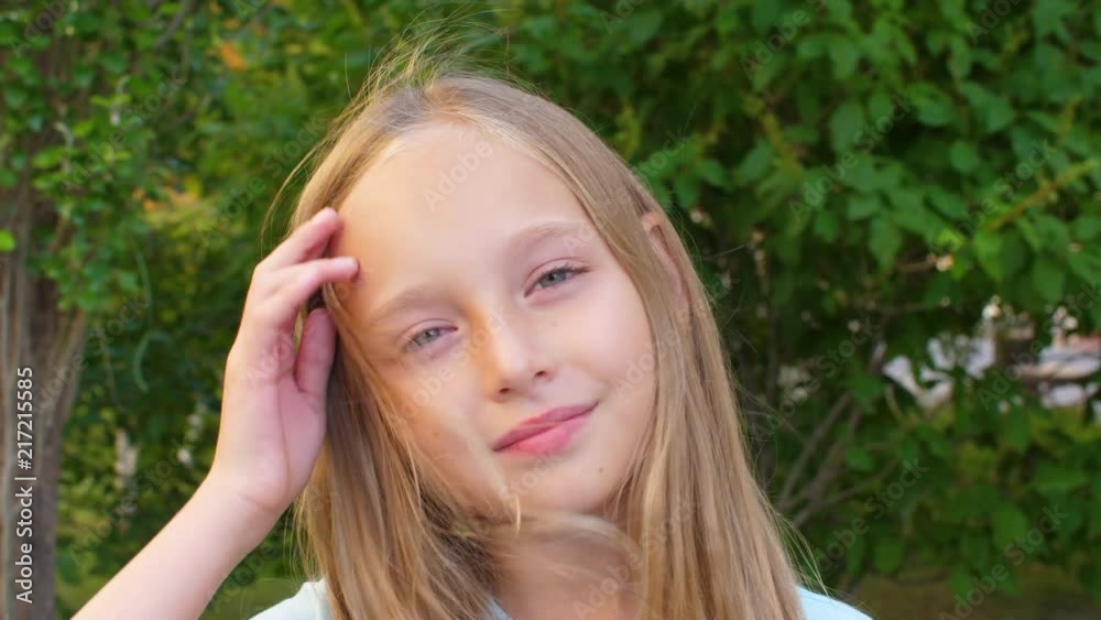 Adorable girl gesturing and touching blonde hair with smile on face