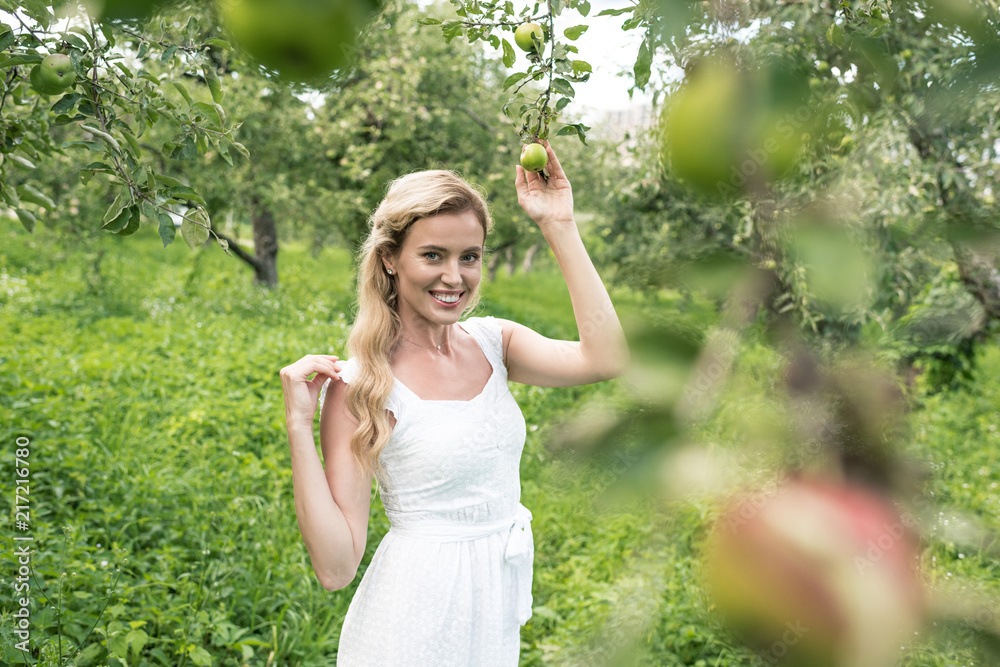 cheerful woman in white dress spending time in apple garden
