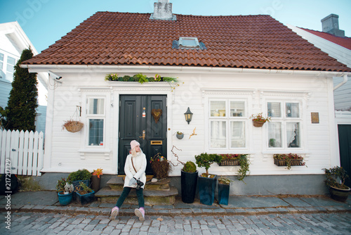 Beautiful young blonde woman in white winter coat sitting on the house porch on sunny day. Cozy house. Architecture. Norway. Stavanger photo