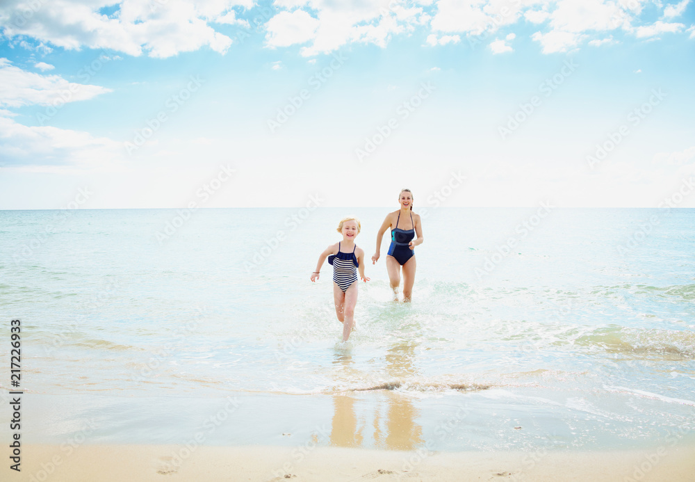 smiling mother and child on seacoast running out from sea