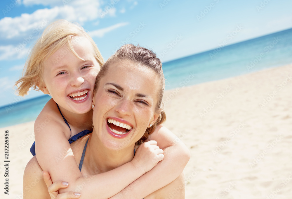 cheerful young mother and child in swimwear on seashore