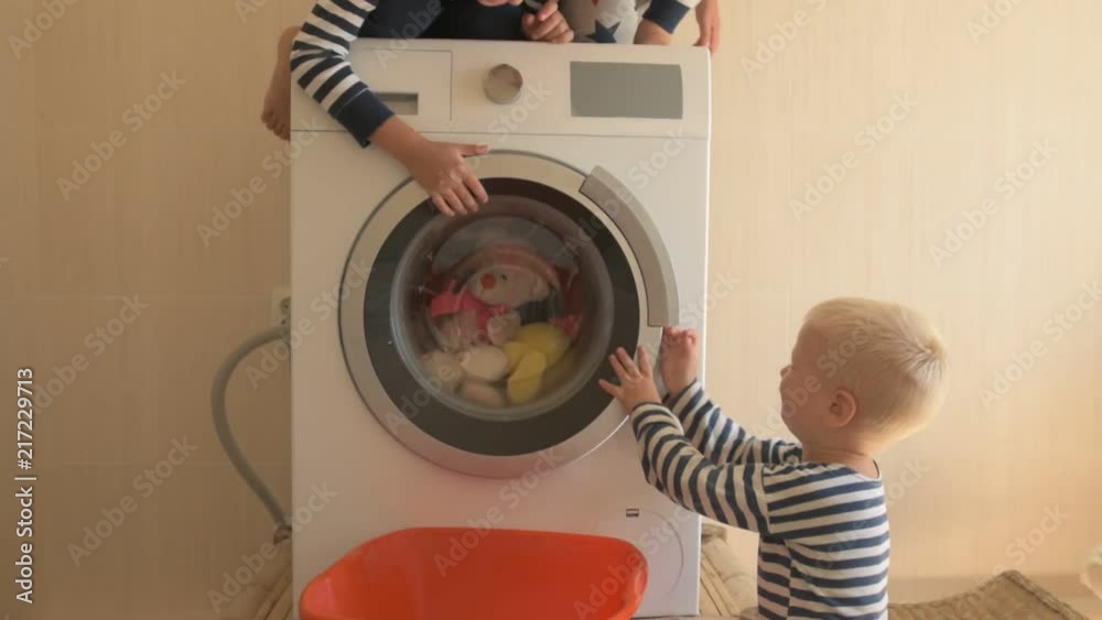 Parents bought new washing machine of new model latest generation. Children try to turn it on and wash soft toys. Three Happy boys are playing at home. Social assistance to large families. Parents bought new washing machine of new model latest generation. Children try to turn it on and wash soft toys. Three Happy boys are playing at home. Social assistance to large families.