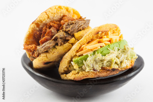 Arepas with two different fillings served in a black ceramic dish on white background