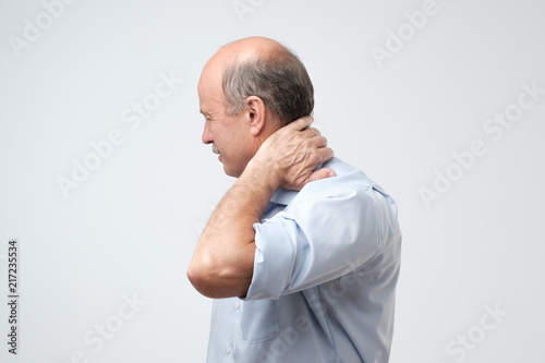 Close up of mature man in blue shirt with closed eyes touching his neck in pain. © Viktor Koldunov