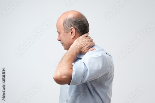 Close up of mature man in blue shirt with closed eyes touching his neck in pain. photo