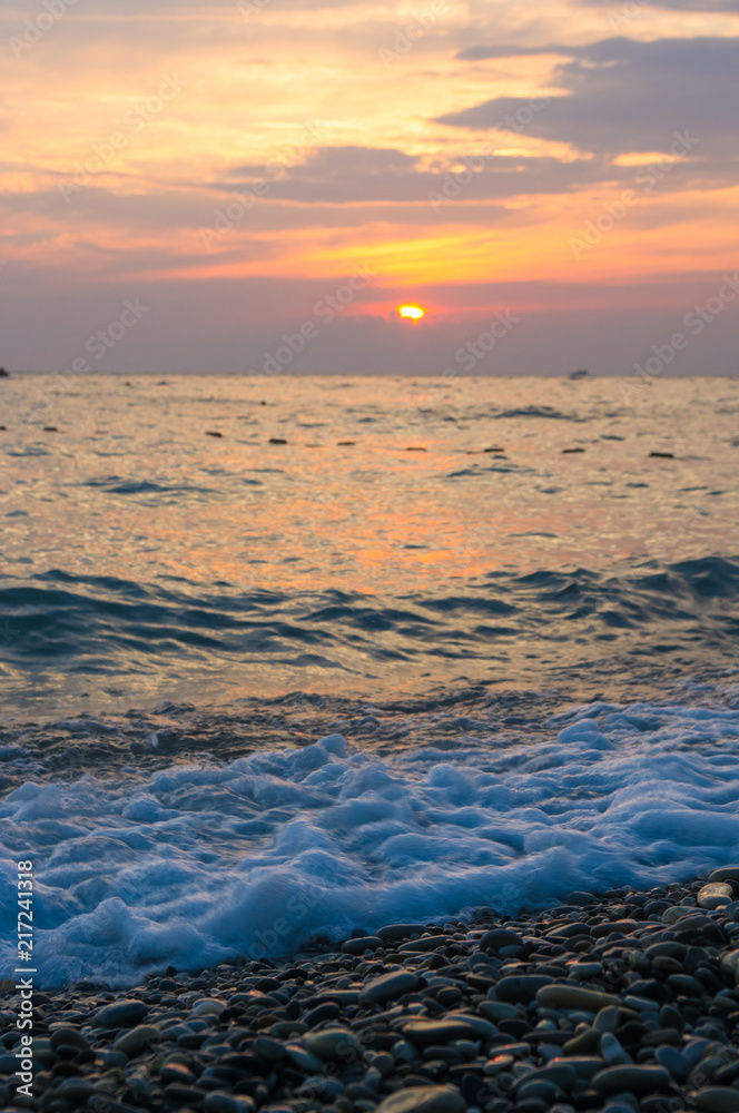 Obraz premium Amazing sea sunset on the pebble beach, the sun, waves, clouds
