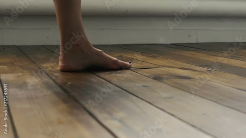 The girl is walking on the wooden floor. Female feet go on the wooden floor.
