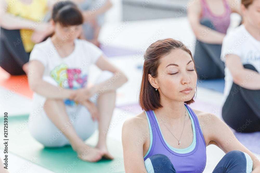 Group of happy cute young women sitting and stretching in yoga asana poses, meditation and workout training concept