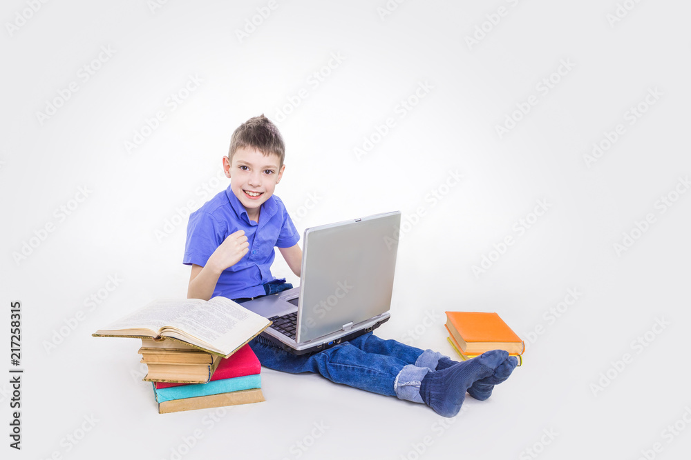 Portrait of cute teen schoolboy sitting near books and typing on laptop keyboard. Happy and surprised little boy, caucasian model isolated on white studio background. Education, study, studying Portrait of cute teen schoolboy sitting near books and typing on laptop keyboard. Happy and surprised little boy, caucasian model isolated on white studio background. Education, study, studying