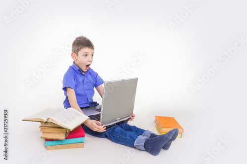 Portrait of cute teen schoolboy sitting near books and typing on laptop keyboard. Happy and surprised little boy, caucasian model isolated on white studio background. Education, study, studying