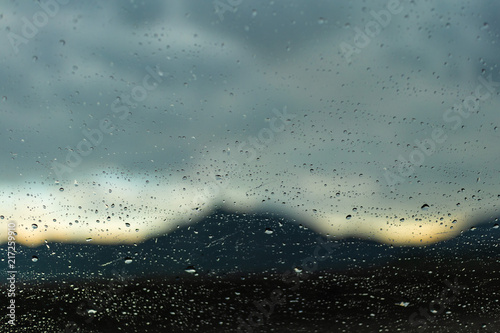 Raindrops on a transparent glass with a blurred mountain landscape