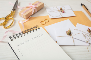 Flat lay and close up view of checklist and wedding invitations on a white wooden tabletop, blank space.