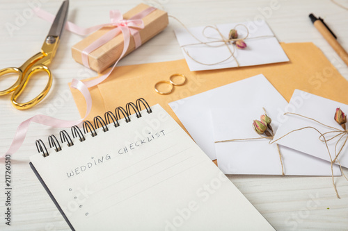 Flat lay and close up view of checklist and wedding invitations on a white wooden tabletop, blank space.