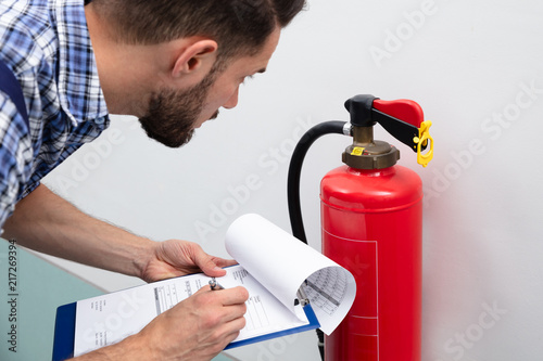 Schilderij op canvas Man Checking Fire Extinguisher Writing On Document