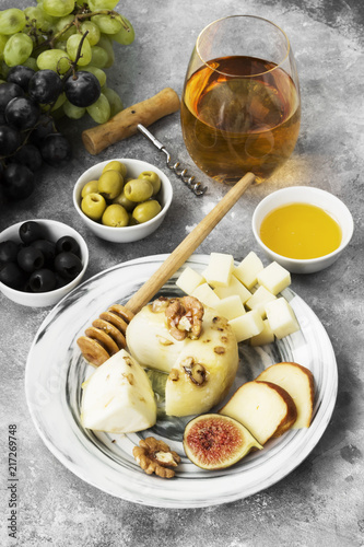 Snacks with wine - various types of cheeses, figs, nuts, honey, grapes on a gray background