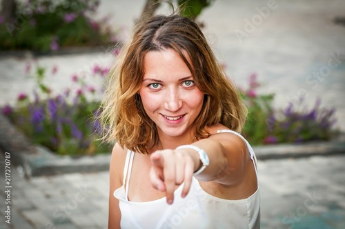 A flirty attractive young Caucasian girl pointing finger at someone, smiling blond girl in a white blouse, I choose you concept, choosy and legible young woman.