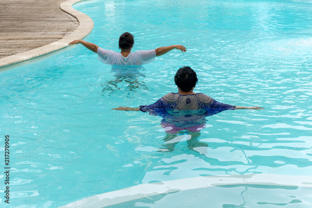 Two senior women doing aqua gym exercise in outdoor swimming pool.