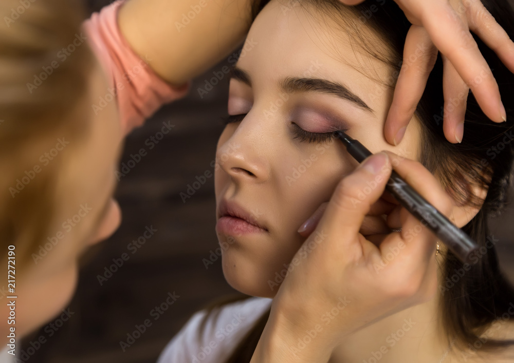 Make-up artist applying liquid eyeliner with brush to beautiful woman face. Make up in process Make-up artist applying liquid eyeliner with brush to beautiful woman face. Make up in process