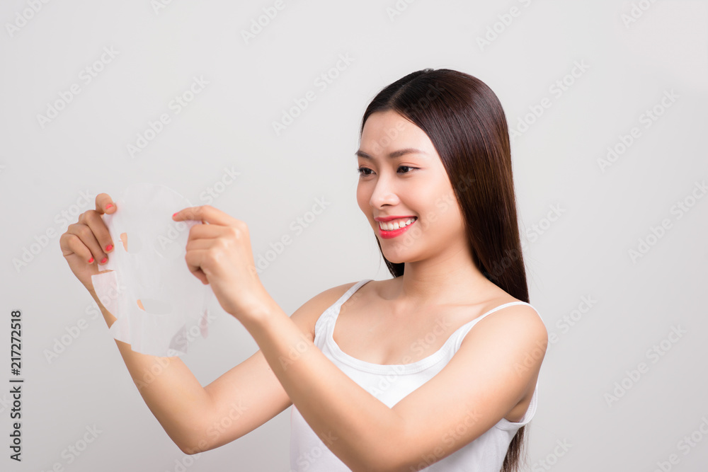 Beauty Skin Care Concept - Beautiful Caucasian Woman applying paper sheet mask on her face white background. Beauty Skin Care Concept - Beautiful Caucasian Woman applying paper sheet mask on her face white background.