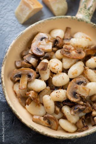 Above view of a serving pan with gnocchi and fried champignons, vertical shot, closeup