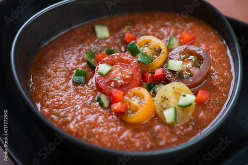Close-up of a cold gazpacho soup topped with fresh sliced cherry tomatoes and chopped cucumber, selective focus