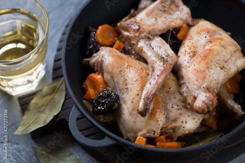 Cast-iron pan with rabbit stewed in white wine with prunes, carrot and onion, close-up