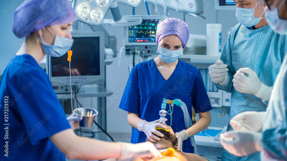 In the Hospital Operating Room Anesthesiologist Applies Anesthesia Mask to a Patient, Assistants Disinfects with Iodine place of Incision, Surgeons Wait to Start Surgery. In the Hospital Operating Room Anesthesiologist Applies Anesthesia Mask to a Patient, Assistants Disinfects with Iodine place of Incision, Surgeons Wait to Start Surgery.
