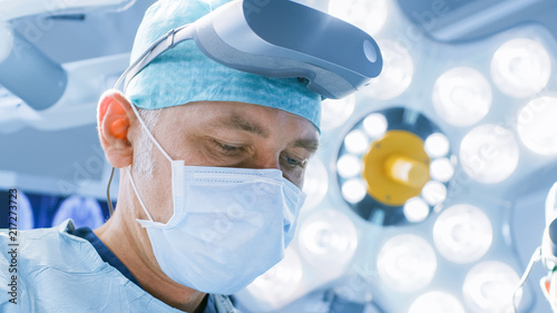 Close-up Shot of a Surgeon with Augmented Reality Glasses Performing State of the Art Surgery in High Tech Hospital. Doctors and Assistants Working in Operating Room.