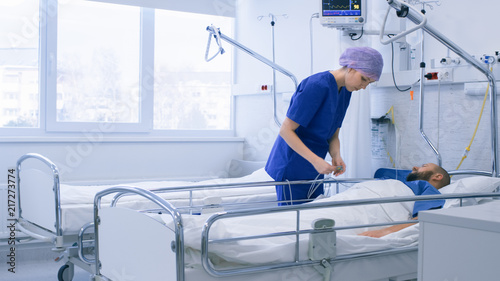 In the Hospital Medical Ward Nurse Takes Care of a Patient Lying in Bed. Clean Modern Hospital with Friendly and Professional Staff.