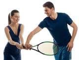 Man gives tennis basic lessons to a young woman, holding racket in a right way. Sharpening skills with a professional coach.