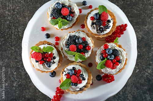 Tasty tartlets with whipped cream and berries on dessert stand, top view