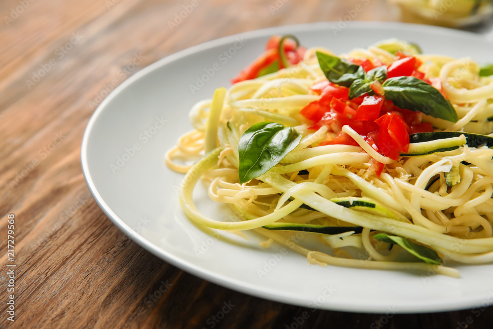 Plate of spaghetti with zucchini and tomatoes on wooden table, closeup