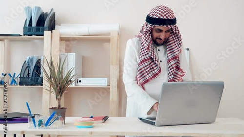a modern Arabic office worker works on a laptop in the office. Muslim dressed in the national ghutra costume. khaliji style of appearance in the office photo
