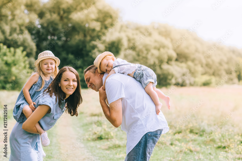 happy parents piggybacking son and daughter in straw hats on summer feild happy parents piggybacking son and daughter in straw hats on summer feild