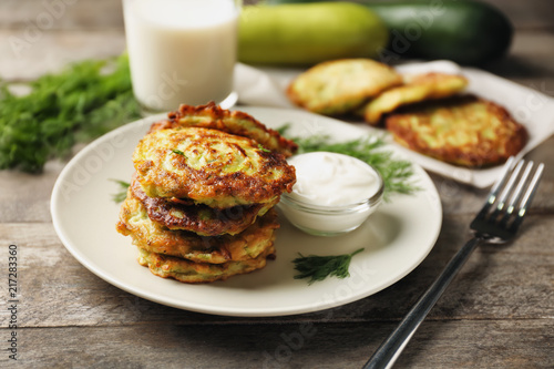 Plate with zucchini pancakes and sauce on wooden table