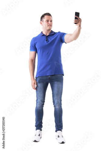 Relaxed young happy man taking selfie photo with smart phone. Full body isolated on white background. 