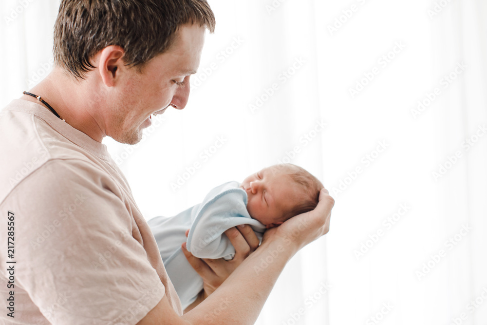 Side view of adult casual man holding tenderly charming newborn baby on hands and looking with love Side view of adult casual man holding tenderly charming newborn baby on hands and looking with love
