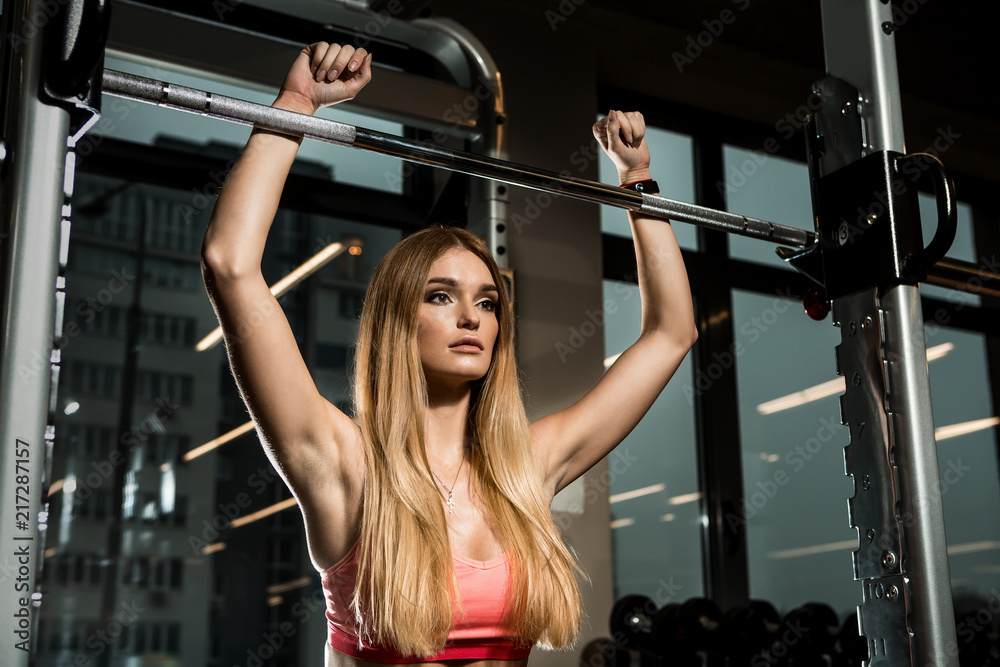 Portrait of sporty brutal athletic young female in fashion sportswear doing functional exercise with heavy barbell. Urban style healthy girl lifestyle and sport concept. Yoga fitness workout at gym.